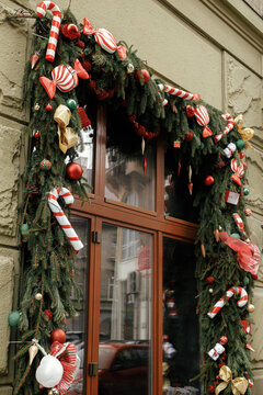 Stylish Christmas Candy Cane, Red Ornaments, Spruce Branches Decoration On Window Or Door Of Building Or Shop. Christmas Festive  Decor For Winter Holidays In City Street. Merry Christmas!