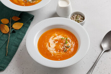 pumpkin soup with seeds and cream in a white plate on a gray table