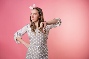 young female pastry chef in a polka-dot apron makes a gesture thumbs down, dislike