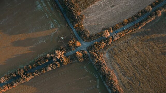 Trucks driving countryside crossroad top view. Autumn country rural road at sunset. Agriculture orange farm fields around. Low traffic transportation. Delivery concept. Aerial drone shot zoom in
