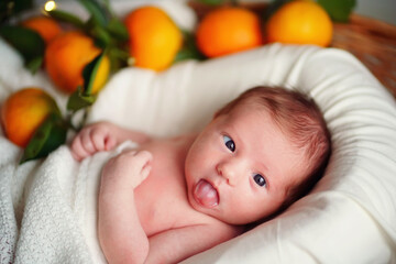Caucasian newborn cross-eyed baby lies in a basket of tangerines under a white blanket. High quality photo