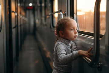 Toddler child looking though train window on sunset, bright sunlight, atmospheric travel by railway...