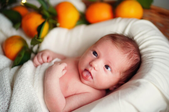 Caucasian newborn cross-eyed baby lies in a basket of tangerines under a white blanket. High quality photo
