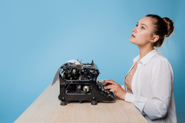 young woman author at a typewriter, writes a text. A writer at a table with a vintage typewriter