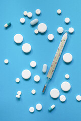 Medical thermometer and antipyretic pills or antibiotics on blue background. Concept of danger and treatment of diseases occurring with high temperature