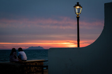 A young loving couple sit in front of a red sunset near the beach