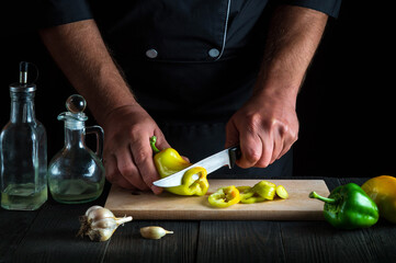 Cook is cutting bell peppers for salad in the restaurant kitchen. Close-up of chef hands while working