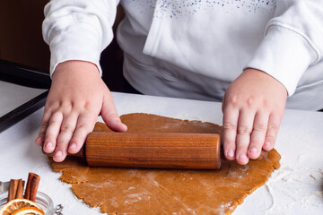 Child rolls out gingerbread cookies dough with rolling pin on table, horizontal, closeup