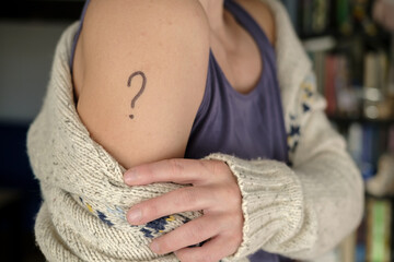 Female shoulder with a drawn question mark. Concept of uncertainty, whether or not to vaccinate against covid-19 and which vaccine to choose. 