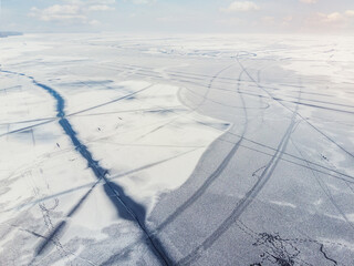 Aerial drone top view of snow covered frozen lake or river surface with big cracked ice diagonal...