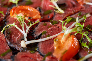 Closeup Beef carpaccio with pesto sauce and tomatoes on black table. Restaurant menu, natural and organic food concept.