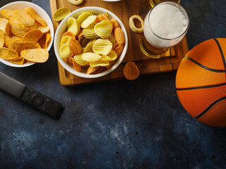 Obraz na płótnie Canvas Potato chips, onion rings, light light beer on a wooden tray, a basketball and a TV remote. Rest in the company of friends, watching your favorite TV shows. Rest, hobbies, relaxation.