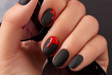 Close up womans hand with halloween manicure on black background holding sunglasses. Manicure,...