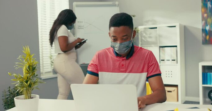 A busy woman stands at the blackboard holding a tablet, searches for the right graphic, prepares a diagram, a man sits at desk entering the data into the system needed to create the diagram