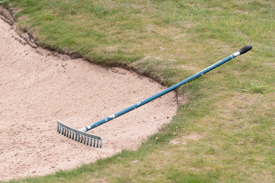 Close up of golf course sand bunker with a rake in the sand.