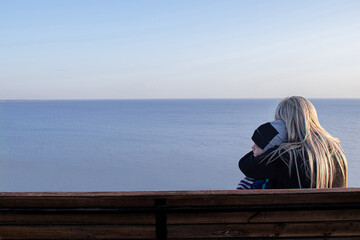 Young mother hugs her son while sitting on a bench against the background of the sea