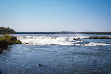 a waterfall in the middle of the forest with blue sky in the background.