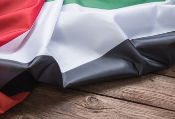 The flag of the United Arab Emirates lies on a brown wooden background with space for text or image.