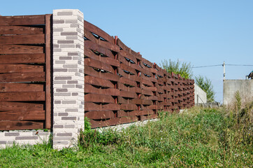 Decorative concrete fence with brick posts near a residential building with a garden.