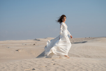 Young woman in white bridal dress walking on sand dunes