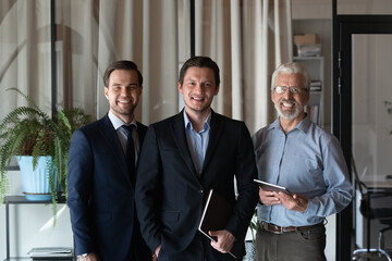 Smiling friendly group of three businessmen of different age private company staff posing for...