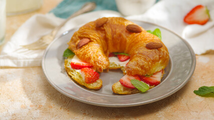 Fresh mouth-watering croissant smeared with butter with fresh strawberries, mint leaves, sprinkled with almonds on a white plate. Home comfort, restaurant, hotel, café, design dishes.