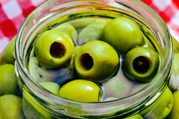 whole green pitted olives in liquid fill large clear glass jar closeup details with red and white...