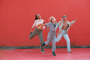 Dancing energetic girls cool moving on red background outdoors. Professional female dancers perform street dance