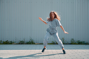 Dancing teen girl showing hip hop dance on urban background. Energetic young dancer cool moving on street