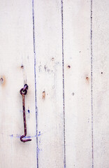 Rusty hook hanging from worn out wall with rusty nails. 