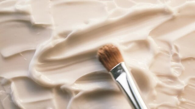 Smearing cream on white background, using brush. Moisturizing balm texture close-up. Makeup and beauty products concept, cosmetics.