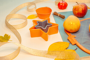 A composition of ribbon, apples, cutting board, orange baking pans, oven mitt, pumpkins, dried oranges and cinnamon sticks.