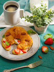 French breakfast - one delicious croissant with butter, fresh strawberries, almonds and milk. Light green background. Daylight. Healthy diet, healthy lifestyle, vitamins.