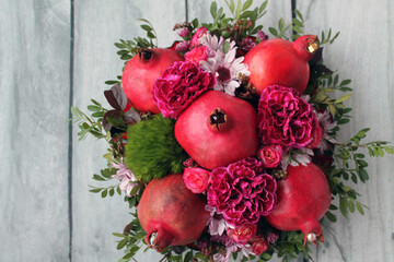 Bouquet with ripe pomegranates and bright flowers on a wooden background. Beautiful flowers or a bouquet is always a good gift or surprise for your friends and family.