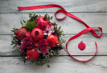 A bouquet with ripe pomegranates and flowers, a small gift in a heart-shaped package and a red ribbon on a wooden background. Flowers and a bouquet are always a good gift or surprise for your friends