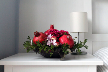 A bouquet of ripe pomegranates and flowers stands in a bright bedroom near the bed. Flowers and a bouquet are always a good gift or surprise for your family and friends