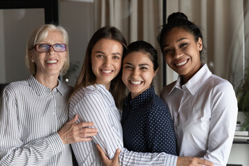 Group portrait of happy friendly business team 4 women of diverse age and race hug smile look at camera. Smiling motivated females teammates colleagues associates enjoy good professional relationship