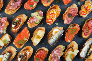 Delicious mixed Spanish tapas with typical specialties on roasted baguette with sesame on a dark...