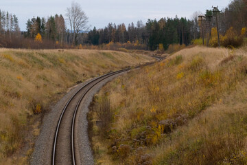 A winding railway track that leads down the hill through a forest valley in autumn.