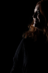 Fototapeta na wymiar Portrait of a red haired woman against black background. Girl in shadows.