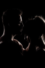 Fototapeta na wymiar Fit couple posing together. Boy and girl side lit silhouettes on black background.