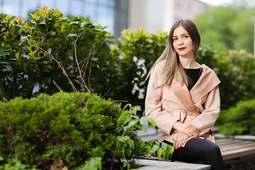 Portrait of a woman sitting on a bench. Successful businesswoman posing outdoors surrounded by green plants.