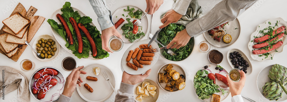 Wall mural Flat-lay of hands eating pork sausages and drinking beer together