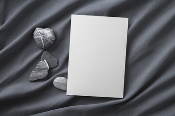 Fototapeta premium Blank greeting card on grey silk and decorating stones. Mockup.