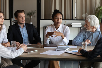 Expressing idea. Diverse multicultural employees sit at conference desk listen to young asian woman speaker. Mixed race lady worker talk to business people of different age gender ethnicity at meeting