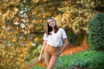 Beautiful girl enjoying autumn. Young woman with autumn maple leaves, season and people concept.