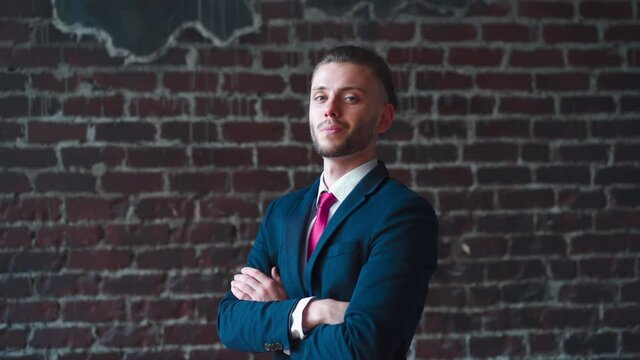 Stylish young businessman portrait standing indoor hands crossed dressed business suit smiling at camera Handsome caucasian male business person red brick wall background serious than smile 