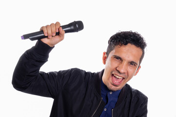 Singing man shouting and looking at the camera. White background. Young latino man singing and looking at camera while holding microphone in his hand.