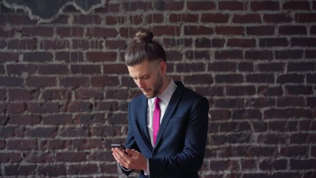 Surprised businessman reading good news on phone indoor red brick wall background. Portrait shoot dancing happy male professional enjoying success. Handsome business man dance dressed business suit 