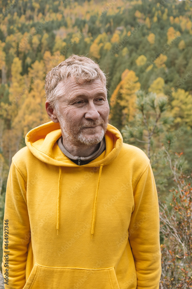 Wall mural An authentic portrait of a handsome unshaven adult male traveler in a yellow hoodie on top of a mountain, against the background of an autumn forest. Selective focus. Close-up. Sustainable environment